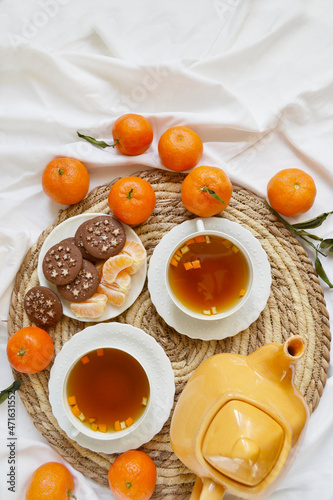Two cups of tea, teapot, mandarins, chocolate cookies on the white bedsheet. Couple winter morning. Tea breakfast service. Cozy, warm atmosphere. Place for text. 