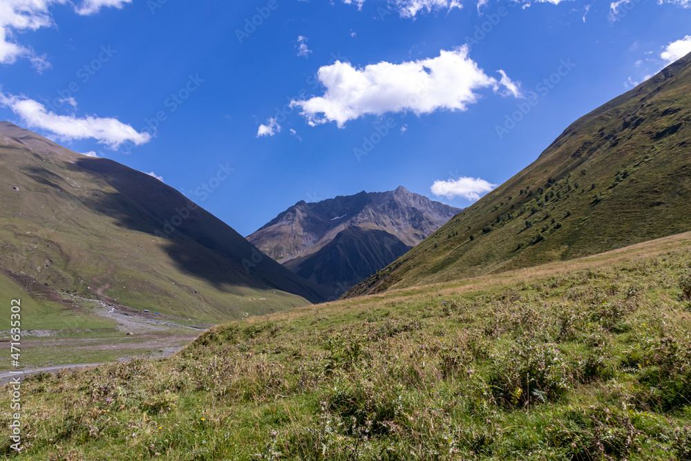 A panoramic view on the high mountain peaks of the Chaukhi massif in the Greater Caucasus Mountain Range in Georgia, Kazbegi Region. A valley with lush green pastures. Wanderlust. Remote location.