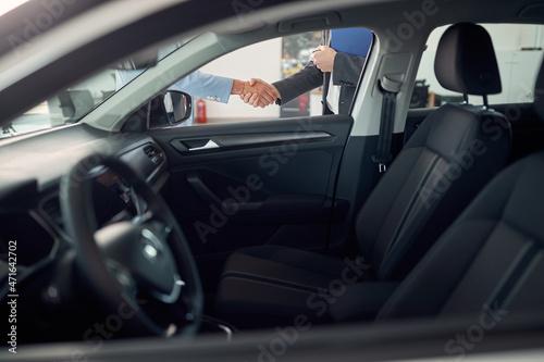 A view through car window on the customer and the salesperson who are handshaking after a new car buy in the salon. Car, shop, buying