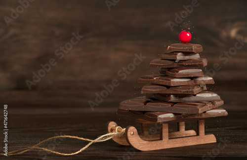 Creative chocolate Christmas tree on small wooden sled on dark wooden background photo