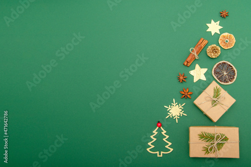 Graphic top view from craft gift boxes, gold circuit of Christmas tree and gold snowflakes, and spices for mulled vine on green background. Copy space