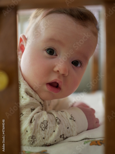 a little girl baby is lying on the crib and looks out of it