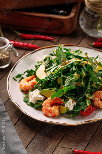 Gourmet shrimp salad with avocado and arugula on wooden background