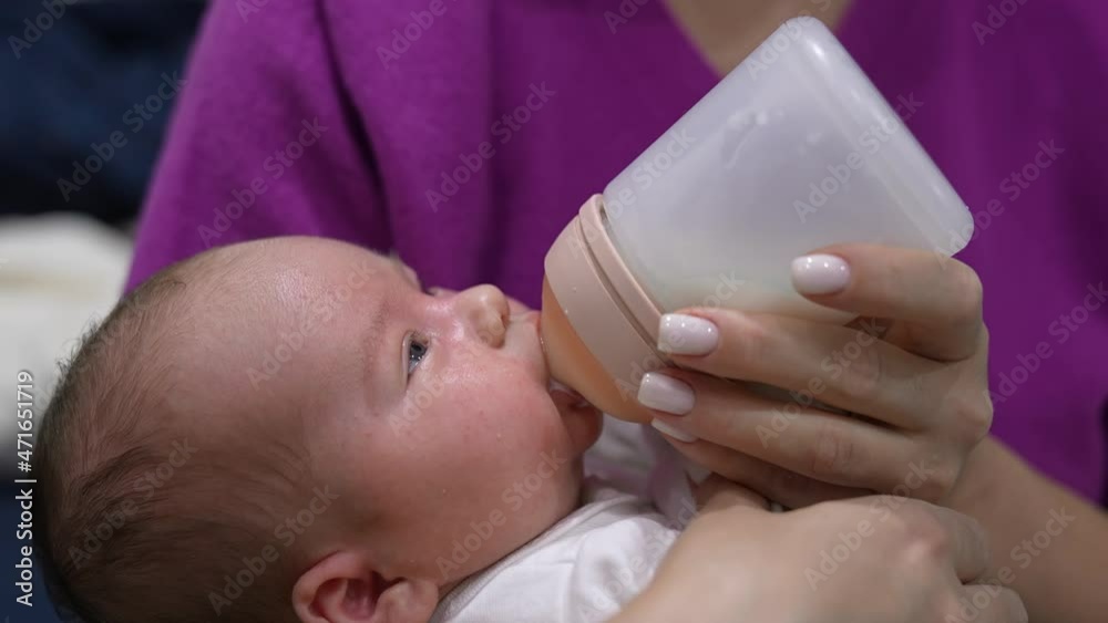Little infant baby lying on mother’s hands. Tiny baby suckling milk from the plastic bottle. Close up shot.