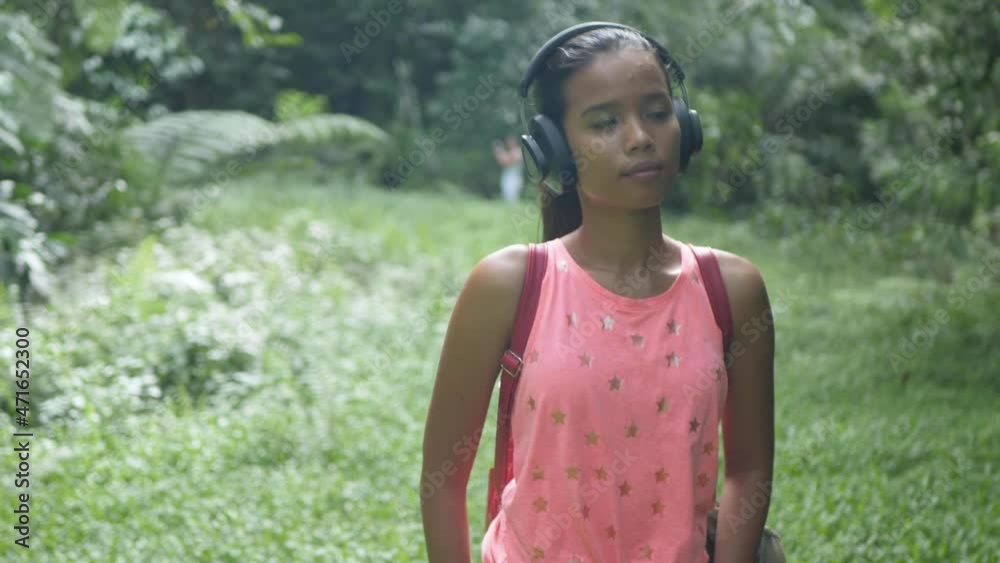 A Young Asian Girl Walks through the Forest, Listens to Music with Headphones, Smiles and Goes forward to the Camera
