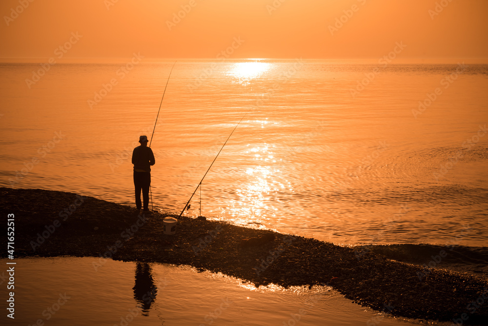 Man fishing in last rays of sunlight on sea shore