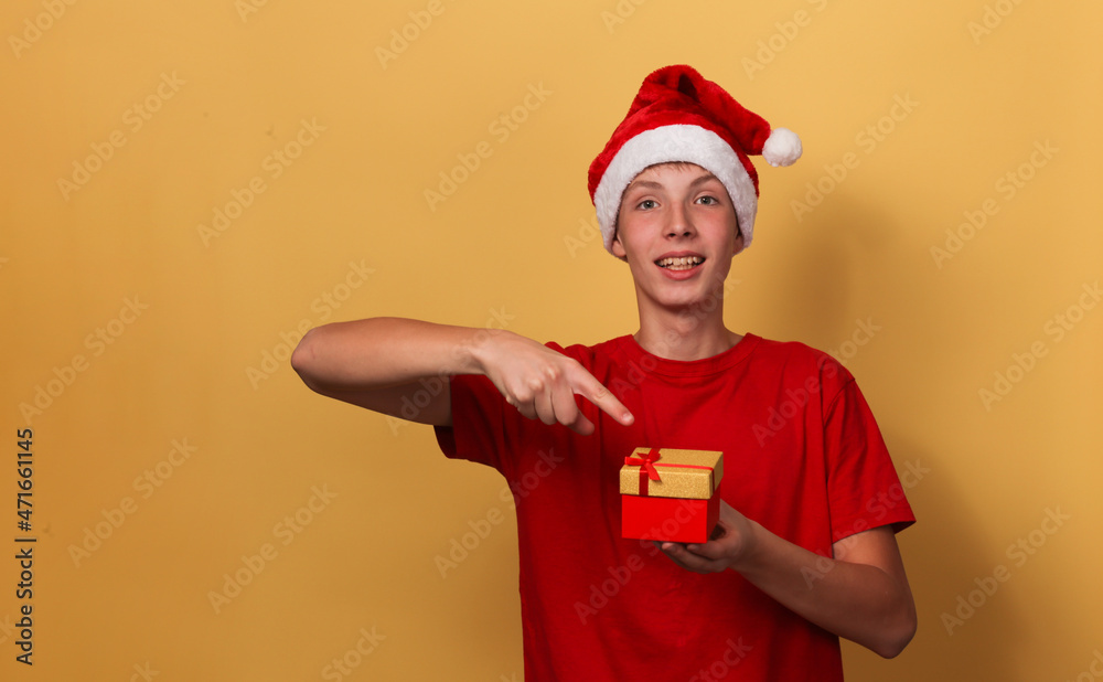 Teenager boy in a Santa hat with a gift box in his hand. Teenager boy in a Santa hat with a gift box in his hand.