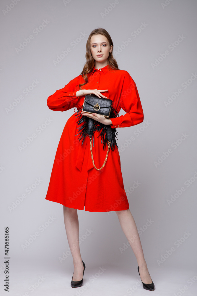 High fashion photo of a beautiful elegant young woman in a pretty red dress, black handbag posing over white, soft gray background. Studio Shot. High fashion photo of a beautiful elegant young woman in a pretty red dress, black handbag posing over white, soft gray background. Studio Shot.