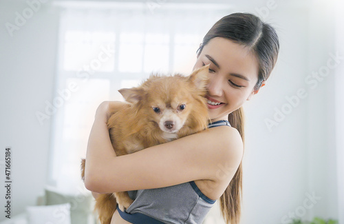Portrait of young attractive asian woman playing with cute lovely dog. Pretty cheerful girl in sport wear with a dog, lifestyle in living room. Owner love pet relax together at home concept