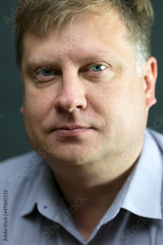 Portrait of a serious adult male blond 40 years old with a blue shirt black background.