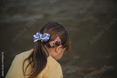 Beautiful hairstyle of child is little side view from behind. Hairstyle of Caucasian little girl close up - brown hair gathered in tail and two bows blue and pink. photo