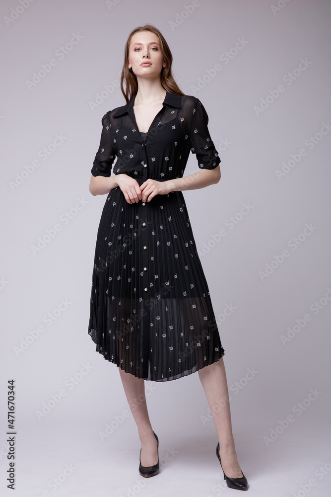 Fototapeta premium High fashion photo of a beautiful elegant young woman in a pretty black dress with small white flowers posing over white, soft gray background. Studio Shot. 