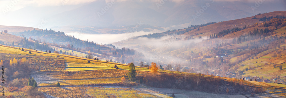 Mountain morning autumn panorama. Colorful fall landscape, foggy sunrise in Carpathians. Majestic misty scenery, valley, village