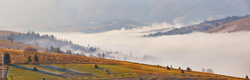 Fall landscape, foggy sunrise in Carpathians. Majestic misty scenery, valley, village, tonal perspective