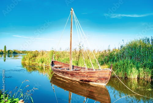 Old wooden fishing boat, green reeds on lake. Wood empty rowboat moored near shore at sunny light day