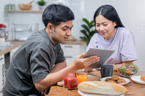 Asian couple looking tablet and working during breakfast time in kitchen