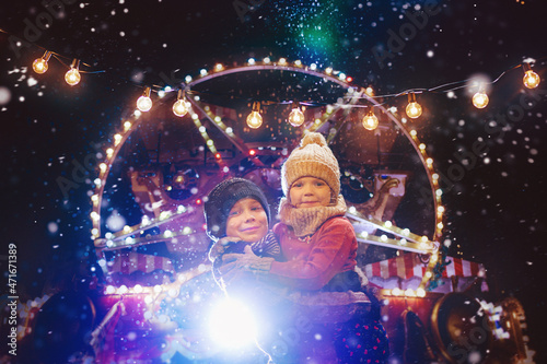 Little cute kids - girl and boy attend the fun fair in the evening at the snow - Christmas market