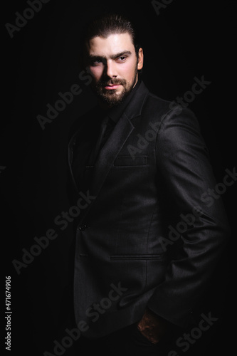 Business portrait of a white caucasian man in a black classic suit on a black background. Bearded man looks confident eyes.