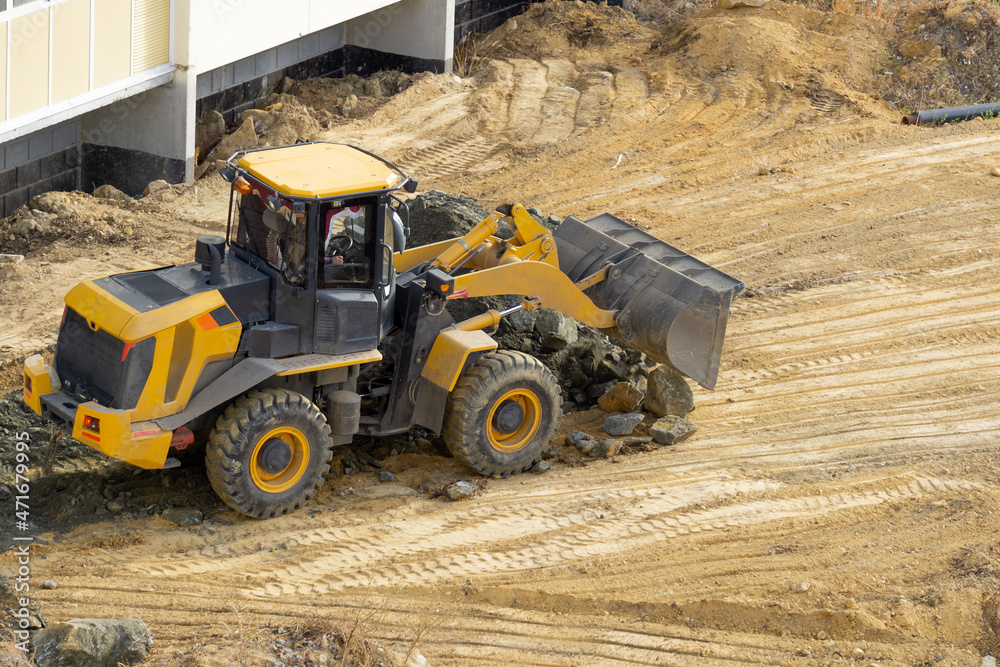 Bulldozer unloads stones at a construction site. A yellow tractor with a bucket conducts construction work. Road construction.