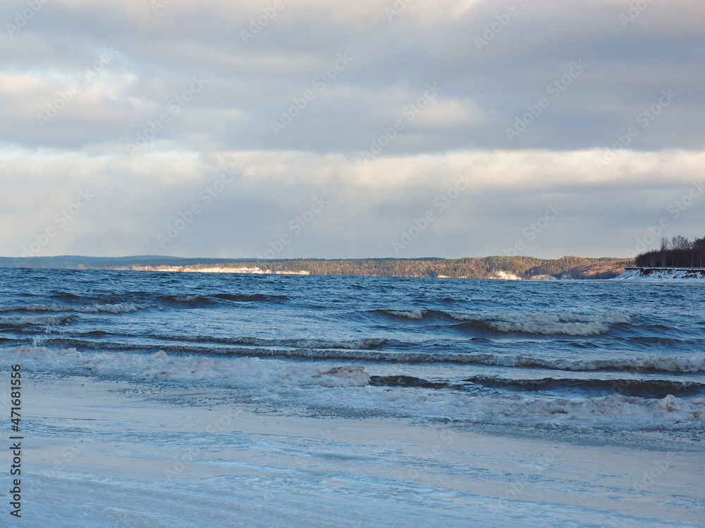 Late autumn on the beach. There are waves on the Kama river. The shore is icy. Russia, Ural, Perm region.