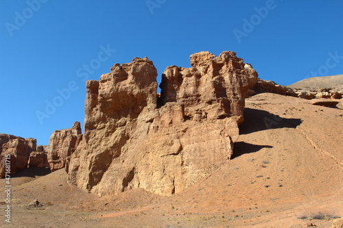 Large relief sandy-clay rock of the red Charyn canyon in Altyn-Emel  mountain slopes  other rocks in the distance  sky with clouds  summer  sunny