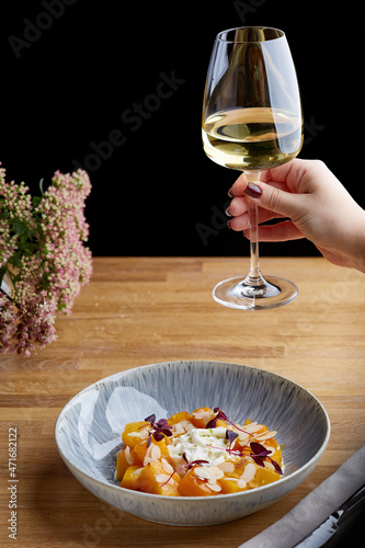 baked pumpkin in ceramic plate on wooden table. Woman hold glass of white wine on background. pumpkin with stracciatella and microgreen