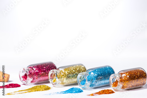 Small Glass jars with blue, pink, orange and golden glitters for nail art and makeup on white background, Copyspace