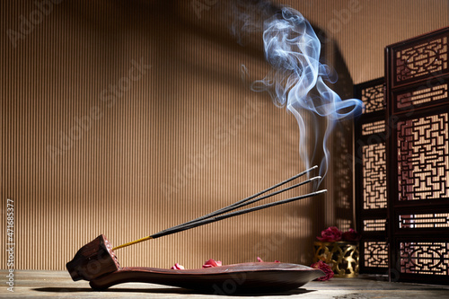 Smoke from burning incense sticks standing on lotus incense holder