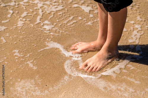 Bare feet in water on sandy beach with jeans