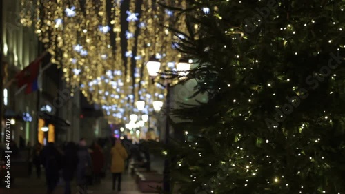 Christmas tree with garlands.New Year holidays illumination outdoor in city street at night. Space full of golden blurry shimmering and waving garlands. Doors of club,casino.Pedestrian silhouettes