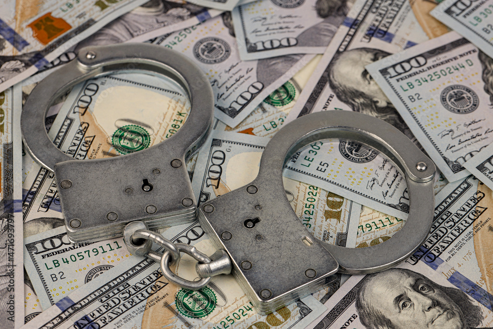 Handcuffs lie on a background of American hundred dollar bills. Concept of anti laundering money ALM. Handcuffs lie on a background of American hundred dollar bills. Concept of anti laundering money ALM.