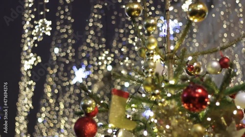 Blurry shimmering abstract holidays background.Christmas and New Year holidays illumination in city street at night. Space full of golden shimmering and waving garlands.Fir tree with balls and toys