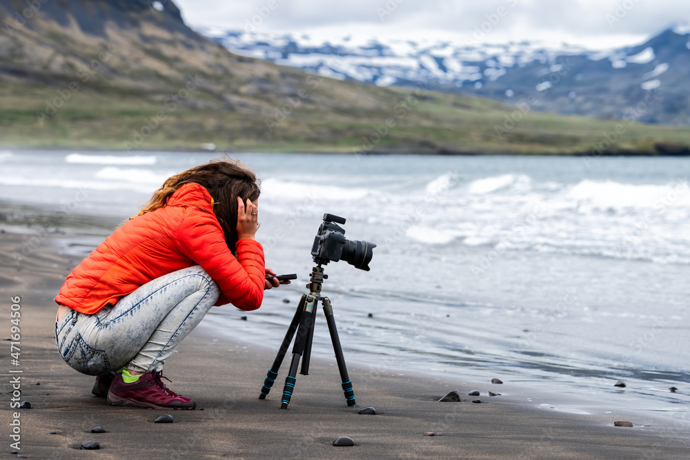 Young girl woman photographer and tripod in Grundarfjordur beach in west Iceland with water waves on shore on Snaefellsnes peninsula