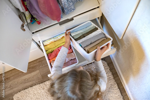 Teenage girl rolled up clothes use Marie Kondo's method. Placing apparel in cupboard photo