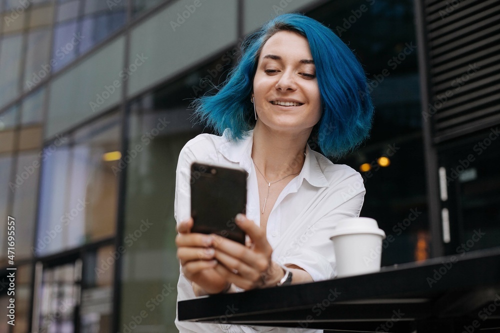 Young charming woman using cell telephone while sitting alone outside coffee shop during free time