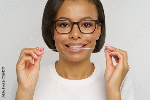 Happy woman holding dental floss for cleaning teeth. African american female with beautiful white toothy smile using thin mint thread isolated over studio wall. Tooth care and oral hygiene concept