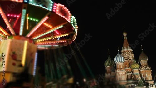 Big carousel on the Red Square in Moscow.Christmas market in the city.People have fun together on holidays.Multicolored flag garland and St. Basil's Cathedral on background