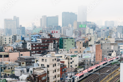 Tokyo, Japan Shinjuku cityscape view buildings on cloudy grey mist fog overcast day with many houses and red metro train with tracks photo
