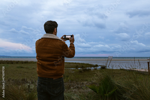 Dramatic and moody back view of a young guy photographing a flood on the beach of Poetto with cloudy sky