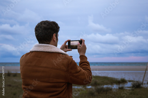 Dramatic and moody close up view of a young guy photographing a flood on the beach of Poetto with cloudy sky
