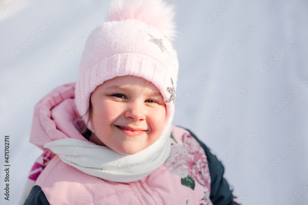 Portrait of little girl on background of snowdrift. Close-up of happy child smiling and enjoying walk in nature on warm winter sunny day. Portrait of little girl on background of snowdrift. Close-up of happy child smiling and enjoying walk in nature on warm winter sunny day.