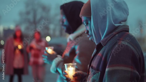 Selective focus shot of two African American men standing outdoors and holding candles in cups while gathering for candlelight vigil