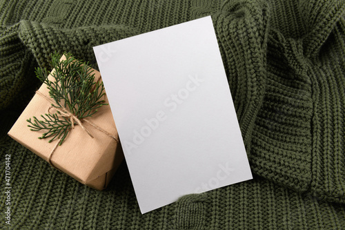 empty 5x7 card mockup kraft gift box with fir decoration on knitted green sweater, design element for wedding invitation, thank you or greeting card. Christmas winter card mock up background