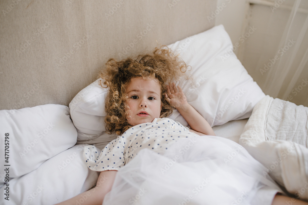 Cute charming curly-haired baby girl lying in bed on a white pillow. Cute charming curly-haired baby girl lying in bed on a white pillow.