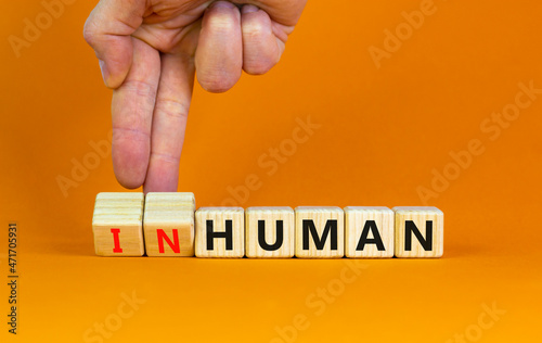 Human or inhuman symbol. Businessman turns wooden cubes and changes the word inhuman to human. Beautiful orange table orange background, copy space. Business, human or inhuman concept. photo