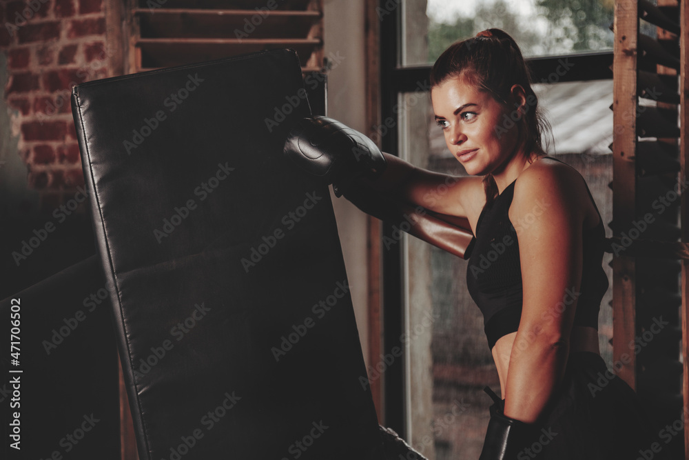 Female boxer is training in ring at punching bag in an old gym