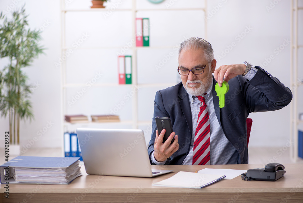 Old male employee holding giant key in the office