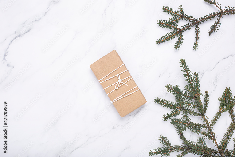Gift and spruce branches on a marble background. Top view, flat lay.