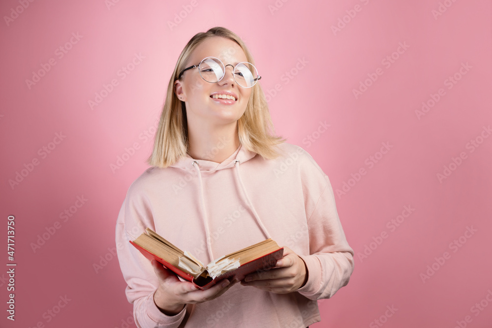 young female student, a portrait with an open book in her hands. Study and gain knowledge, preparation for admission to college or university, exams. Cute blonde with glasses and a pink hoodie. young female student, a portrait with an open book in her hands. Study and gain knowledge, preparation for admission to college or university, exams. Cute blonde with glasses and a pink hoodie.