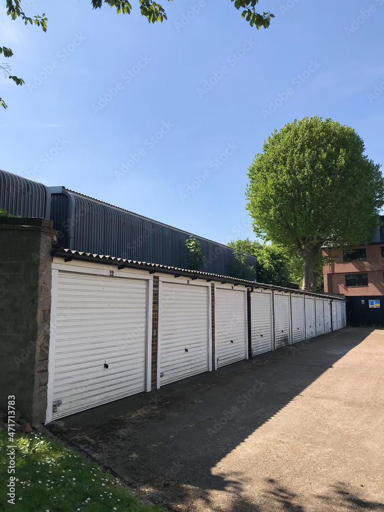 London, England - May 8 2020 - A row of closed white parking garage doors in suburban London, under a sunny blue sky.  Image has copy space.